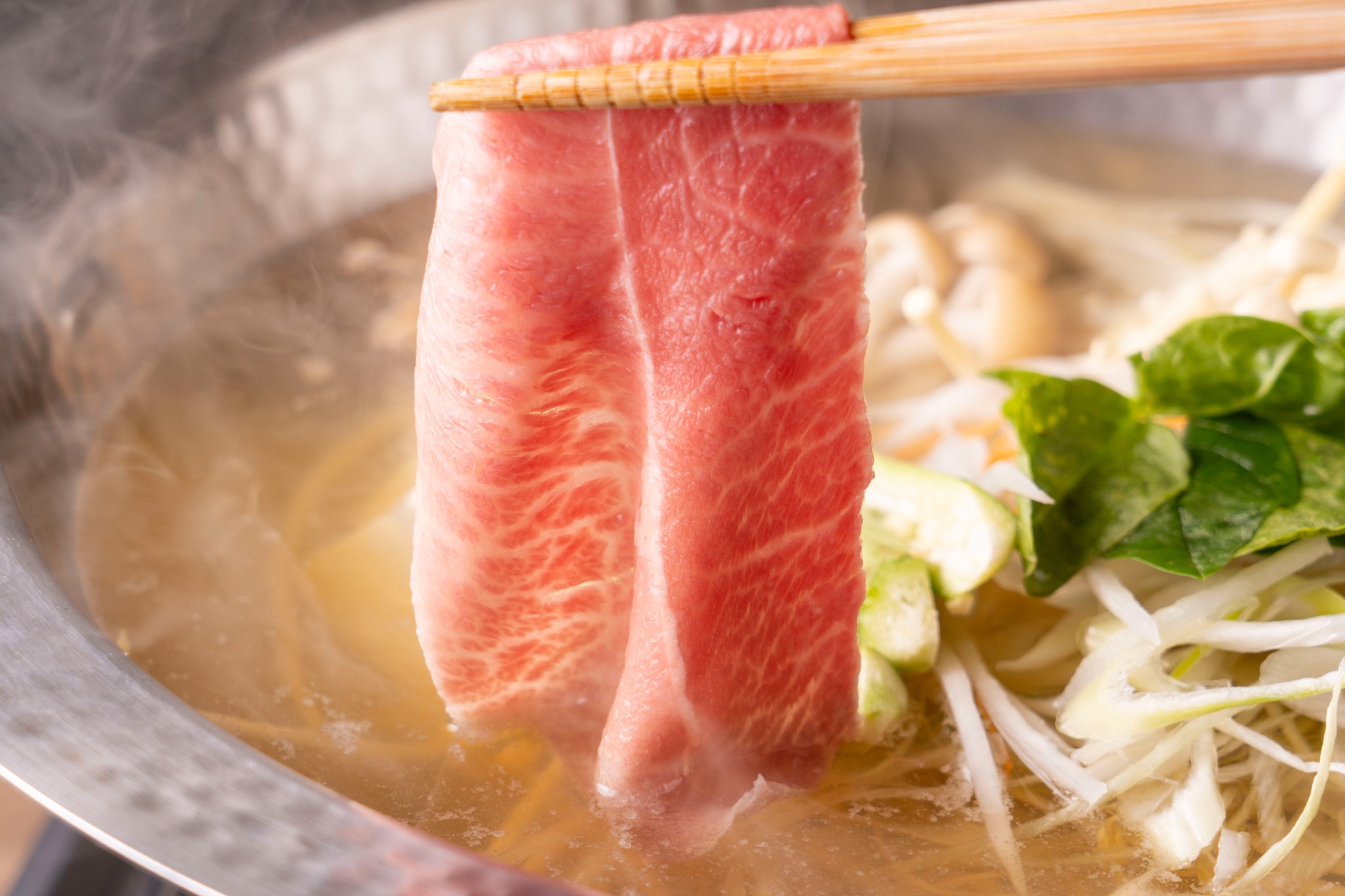 湯気の立つ鍋の上に、箸で持ち上げた霜降りの肉